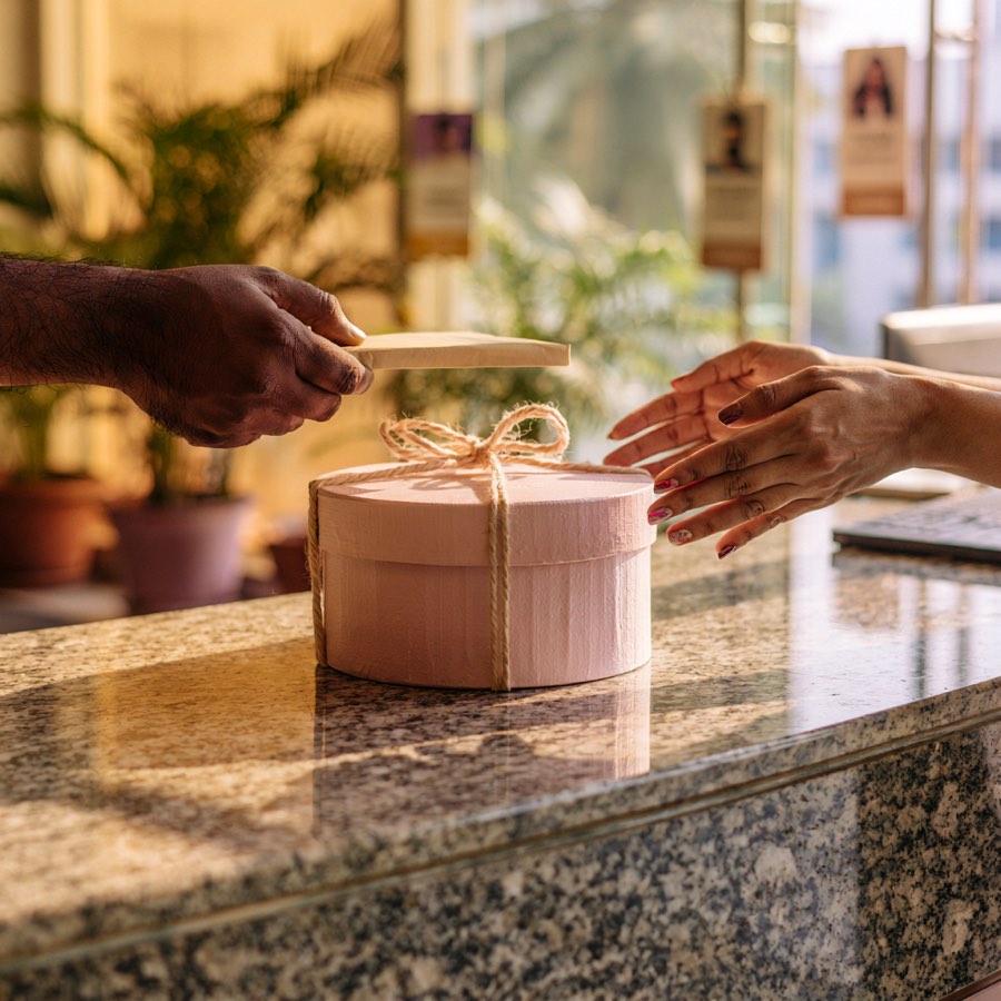 A pink cake box tied with string, handed across a granite reception desk in morning light